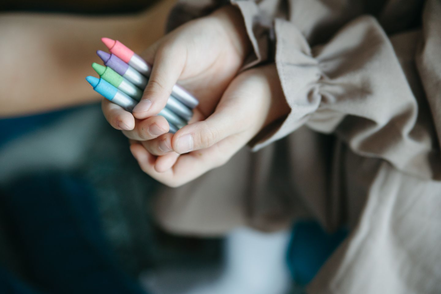 Hands holding blue, green, purple, and pink crayons.