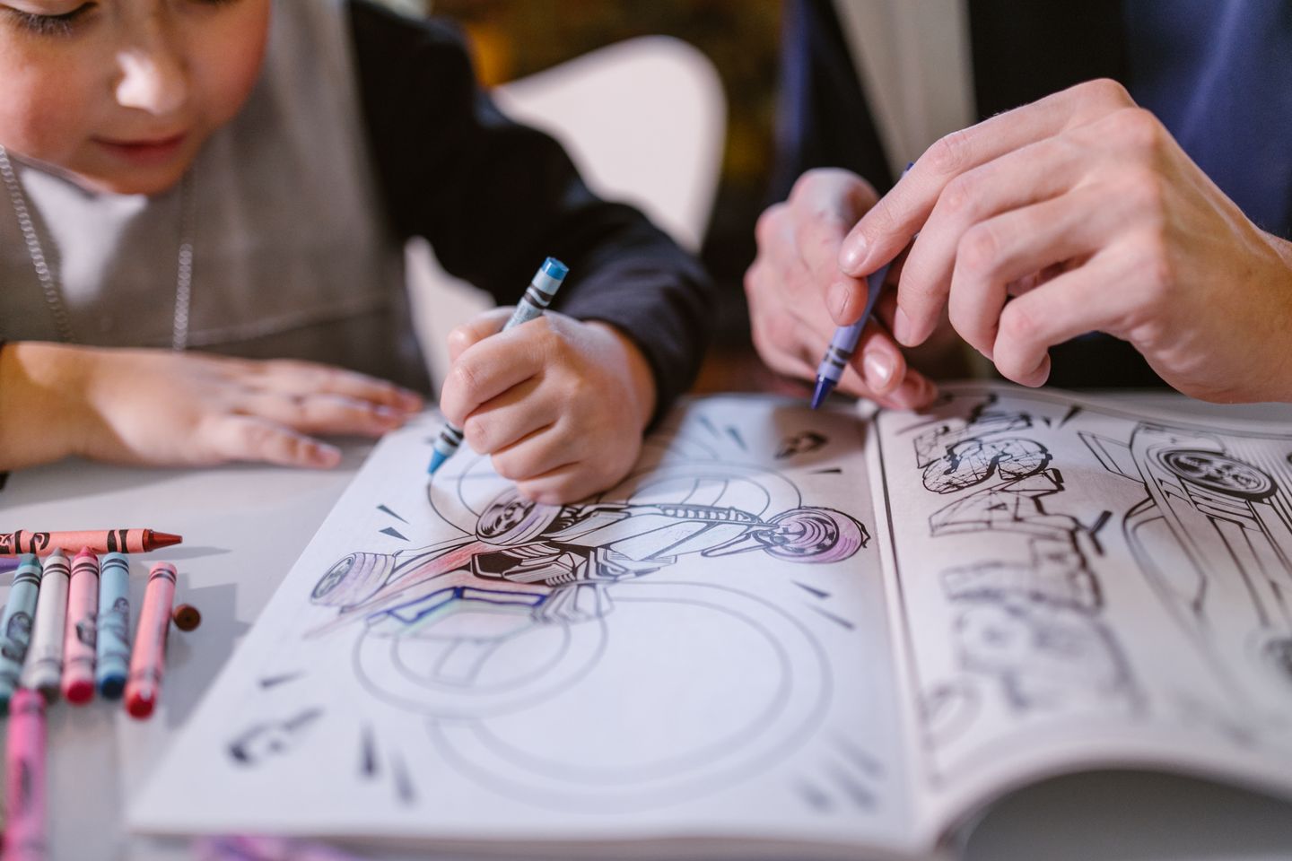 A child and adult use crayons to color a motorcycle picture together.