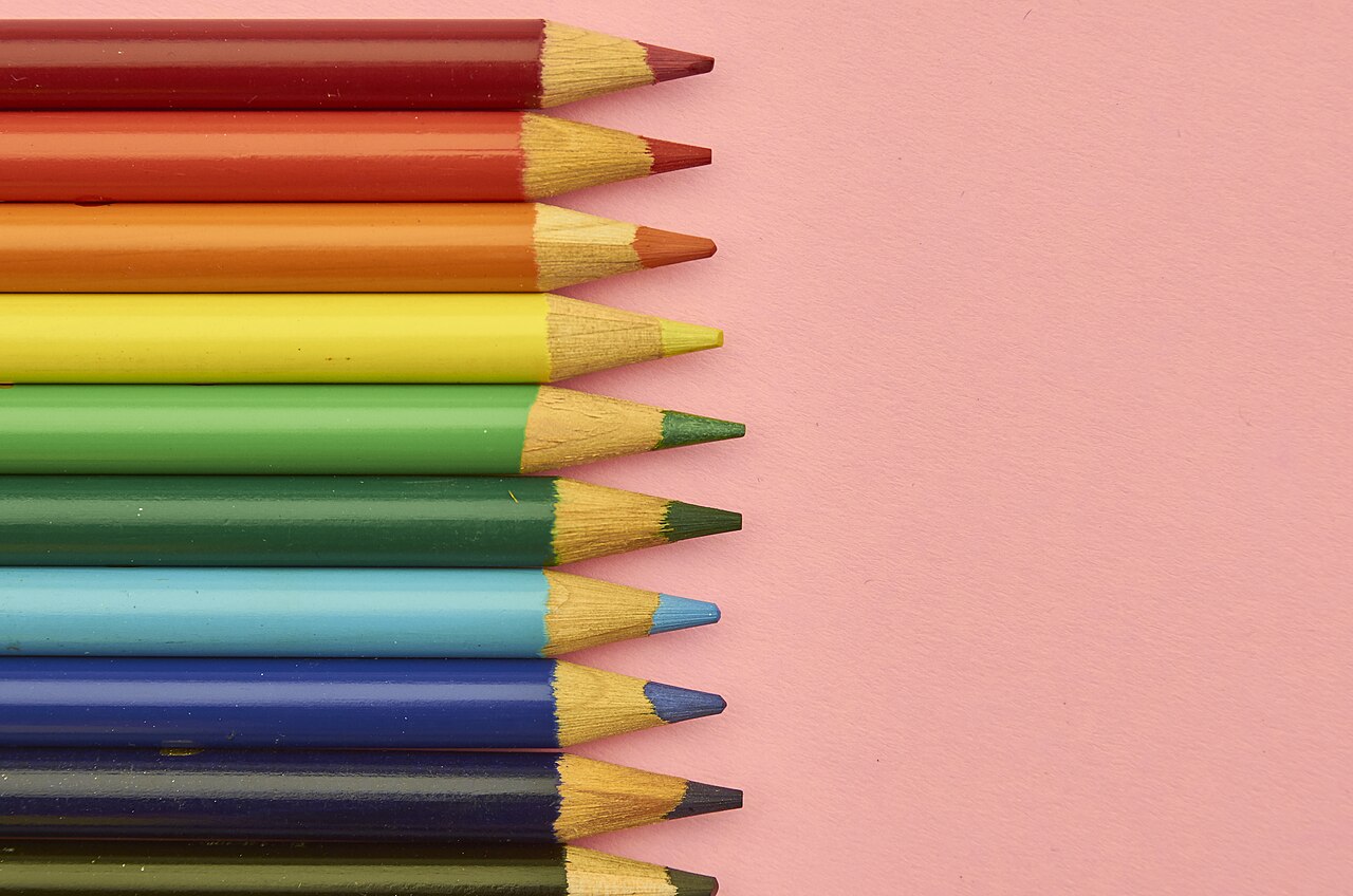 A row of sharpened rainbow-colored pencils on pink paper.